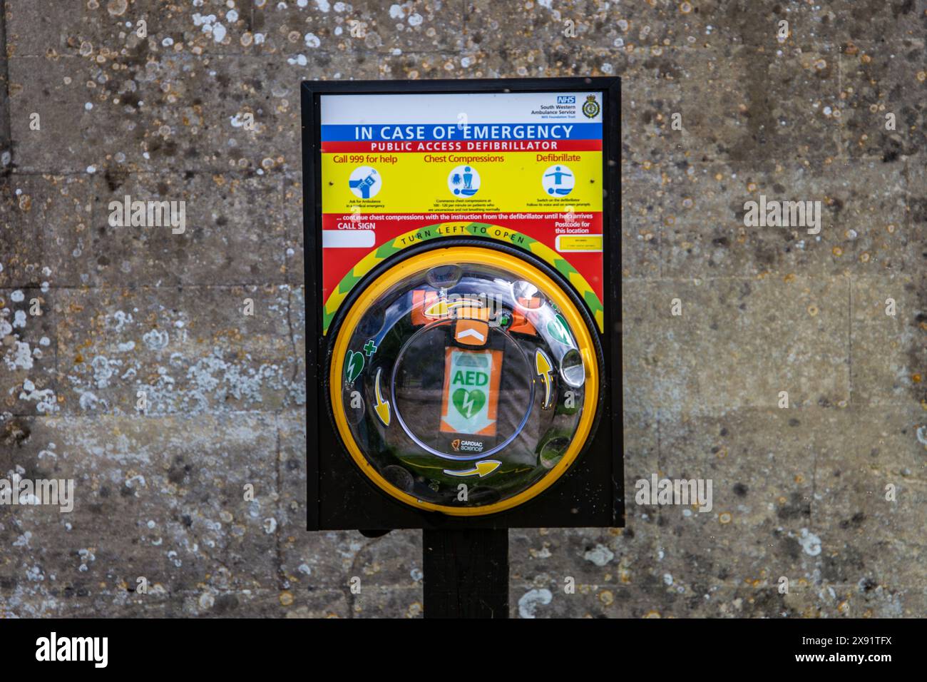 Défibrillateur d'accès public dans un boîtier jaune monté sur le bureau devant un mur texturé avec des instructions d'urgence. Banque D'Images