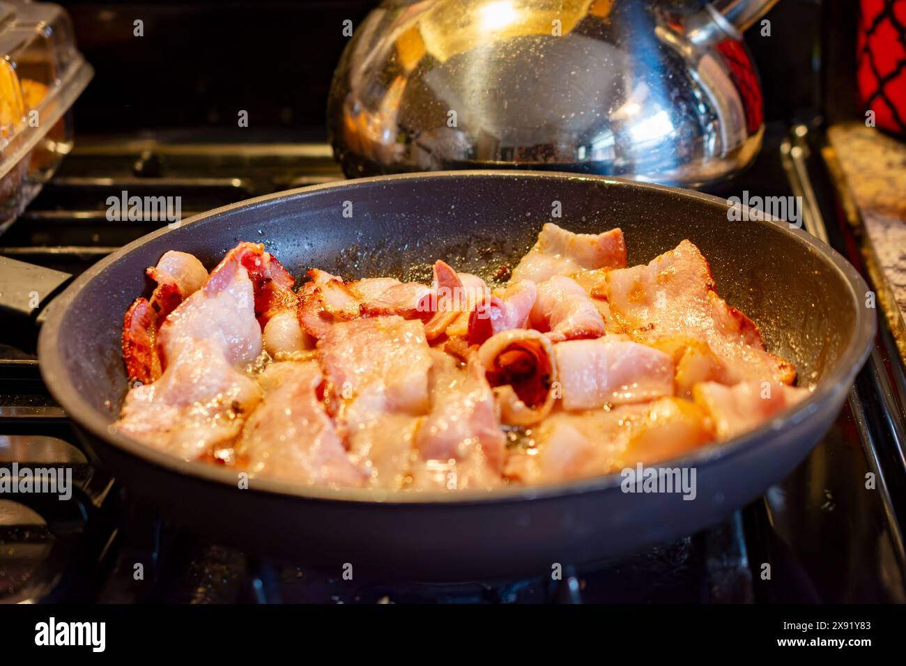 Une livre de frites de bacon coupées épaisses dans une poêle sur une cuisinière à gaz. Banque D'Images