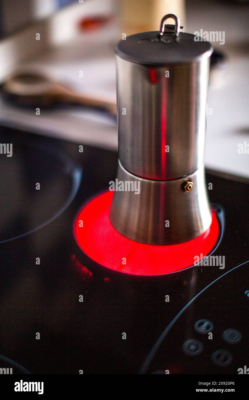 Un pot de moka en acier inoxydable chauffe sur une cuisinière à induction en céramique à éclairage rouge, préparant du café en Espagne. Banque D'Images