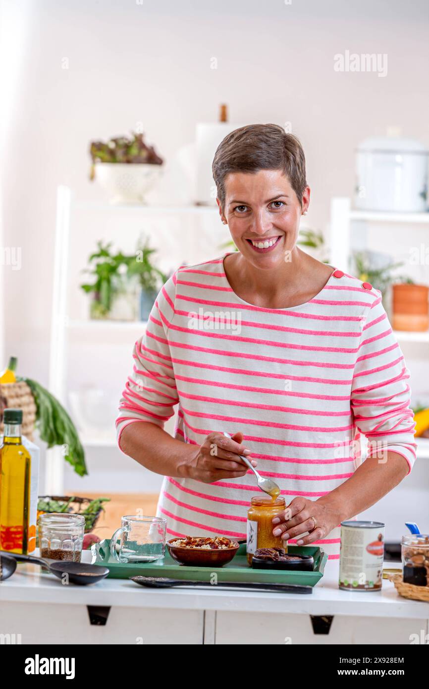 Jeune femme avec un pot de miel pour le mélanger avec des céréales et d'autres graines. Préparation dans la cuisine d'un petit déjeuner végétarien sain 016643 075 Banque D'Images