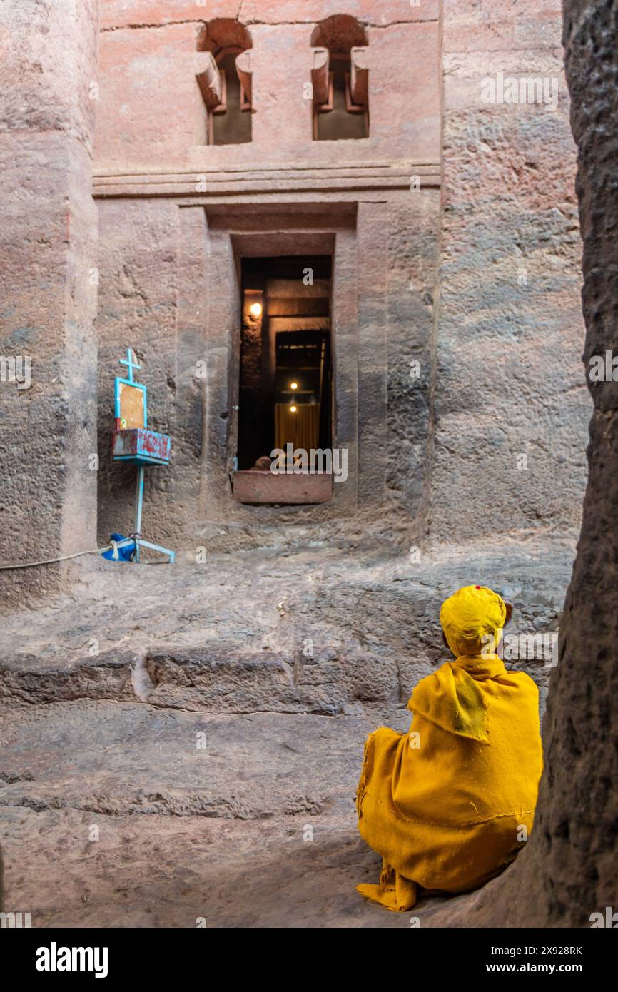 Femme aînée pèlerine en jaune à l'entrée de l'église ortodoxe monolithique taillée dans la roche de Bete Medhane Alem, Lalibela, région d'Amhara, Ethiopie. Banque D'Images