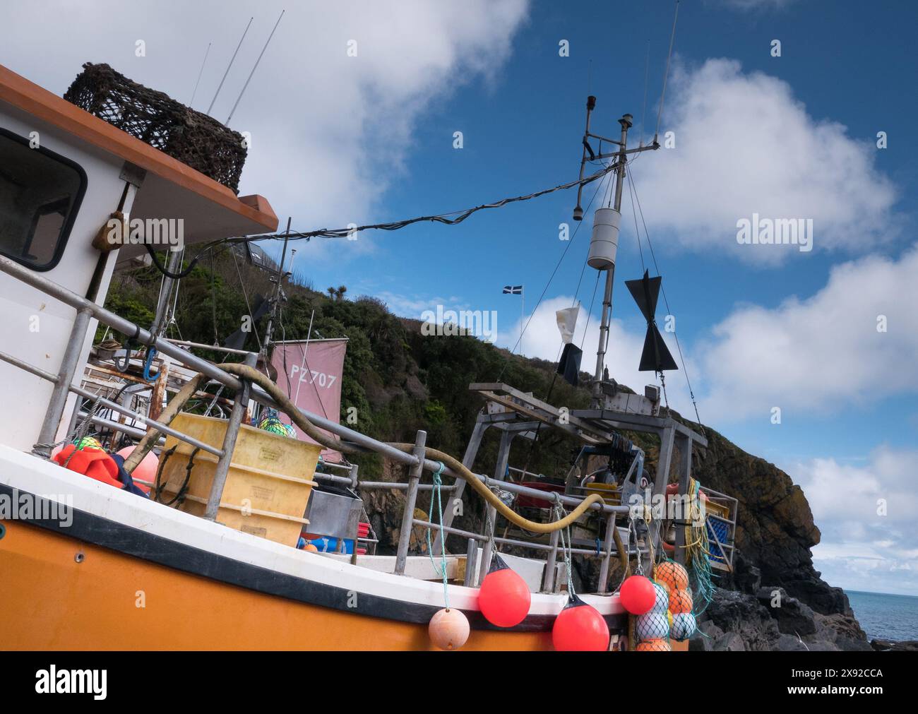 Cadgwith Cove bateau de pêche avec drapeau St Pirans volant sur les falaises ci-dessus Banque D'Images