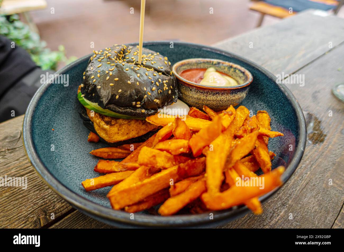 Burger noir avec frites sur fond de bois servi sur une assiette en céramique bleue Banque D'Images