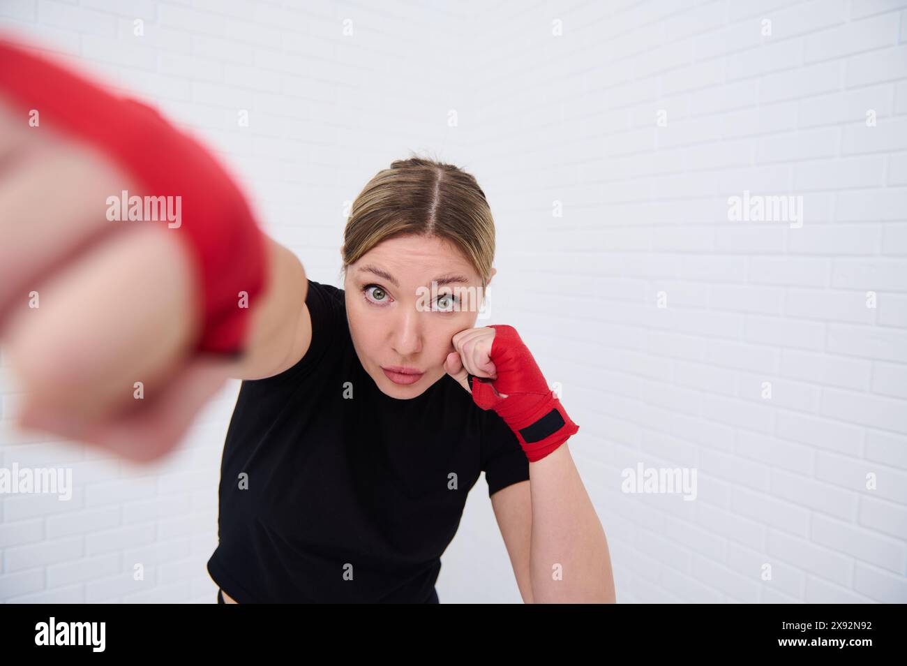 Combattante déterminée avec des bandes rouges sur ses poings, pointant vers l'avant regardant la caméra, isolée sur fond de mur blanc. Jeune femme boxeur 40 s. Banque D'Images