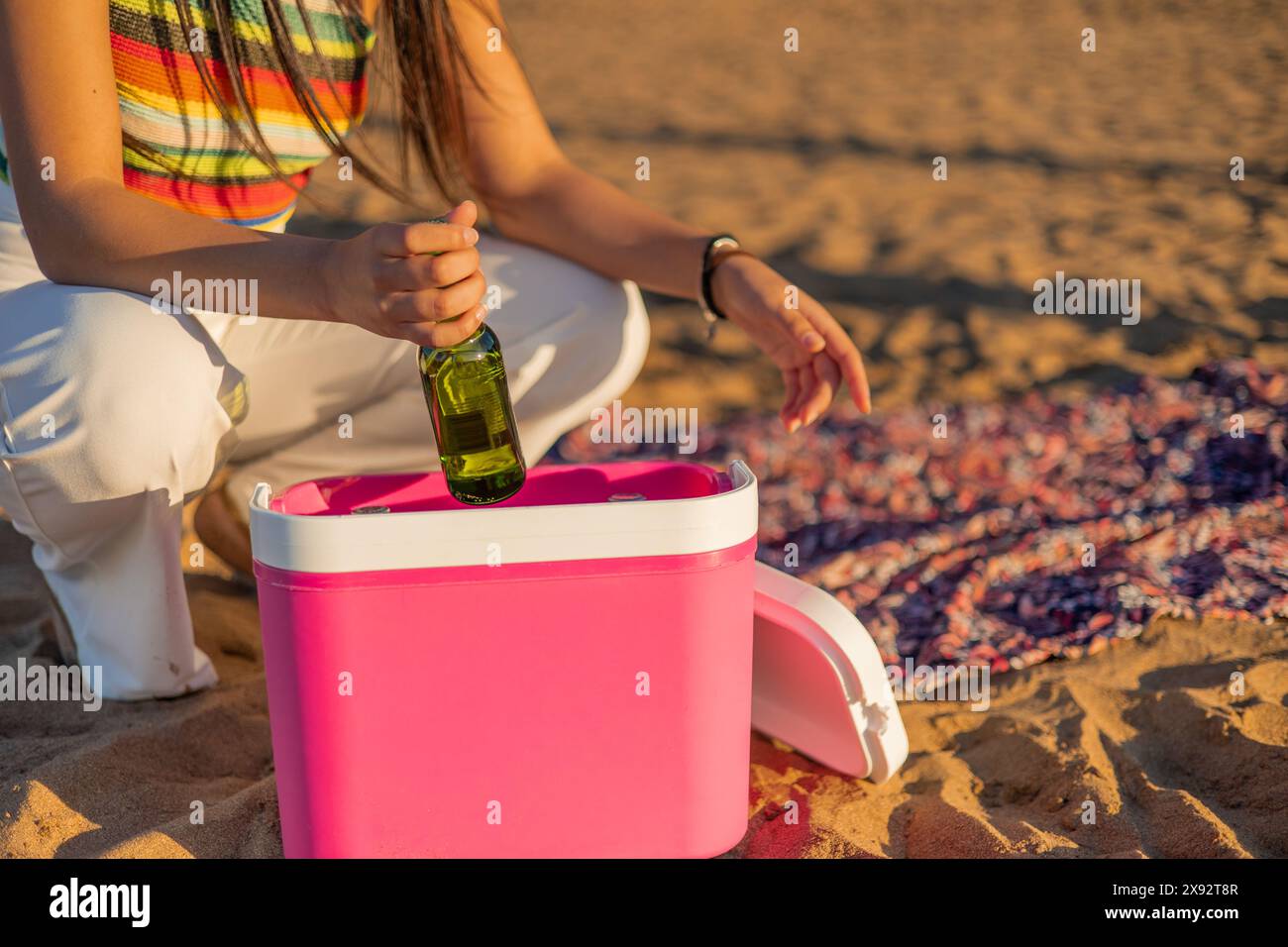 femme non identifiée profite du coucher de soleil d'été sur la plage tout en récupérant une bière froide d'une petite glacière portable. Son anonymat s'ajoute à l'univers Banque D'Images