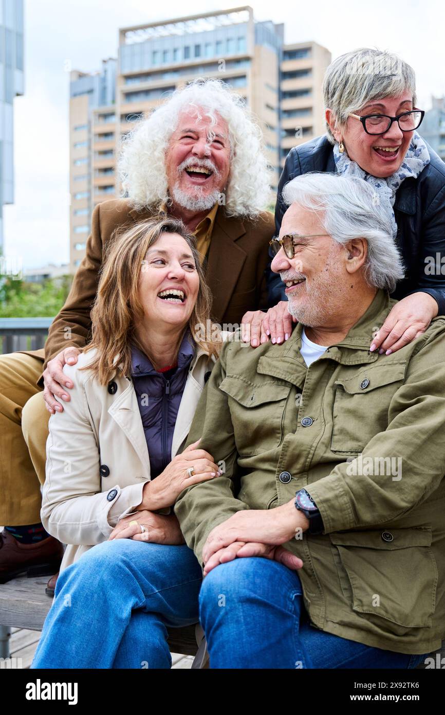 Groupe de vieux Caucasiens amis les gens s'amusant à rire ensemble assis sur le banc en ville. Banque D'Images