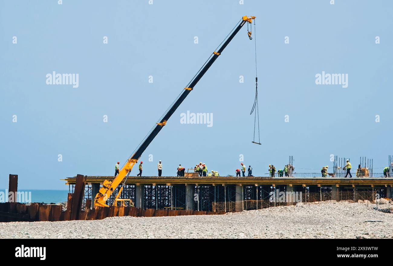 Constructeurs et ouvriers en vestes jaunes sur le chantier de construction sur la jetée de mer sur la côte. Grue de travail au premier plan. Batumi, Géorgie. Photo de haute qualité Banque D'Images