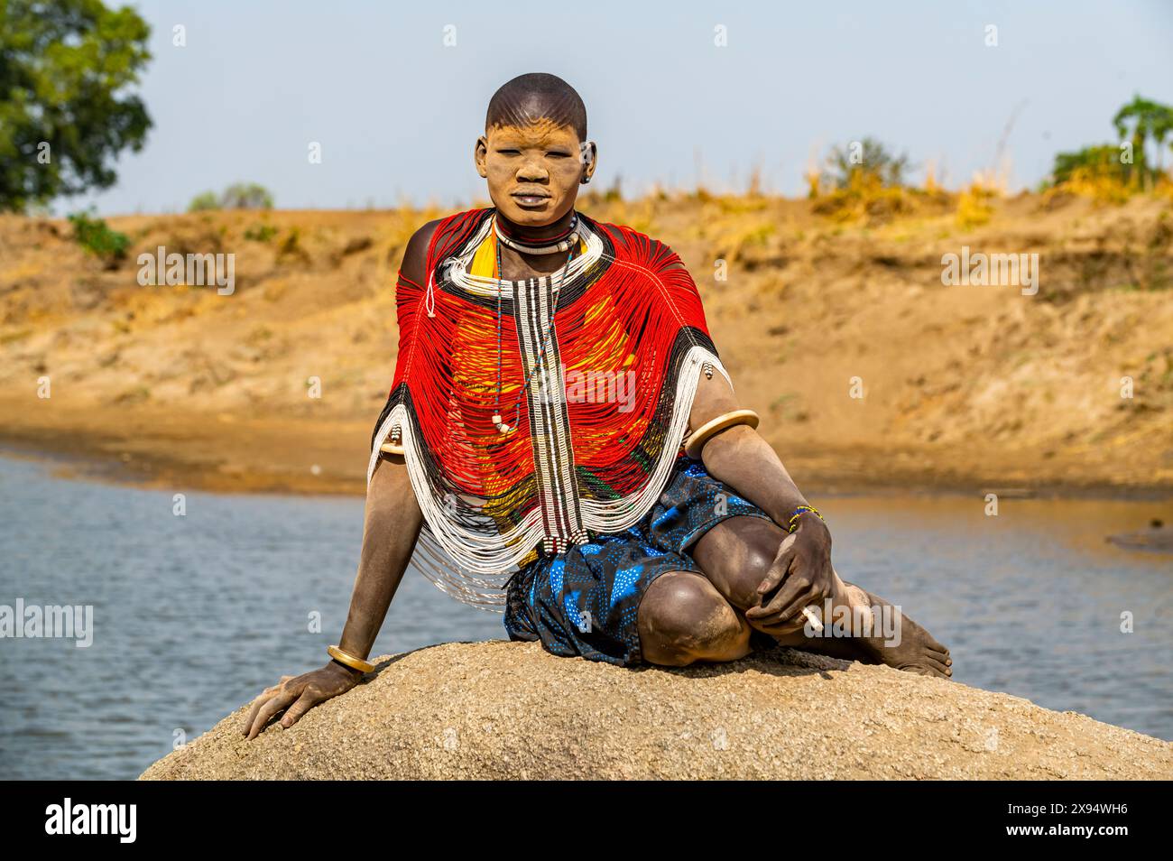 Femme Mundari dans une robe traditionnelle avec le visage couvert de cendres posant sur un rocher, tribu Mundari, Soudan du Sud, Afrique Banque D'Images