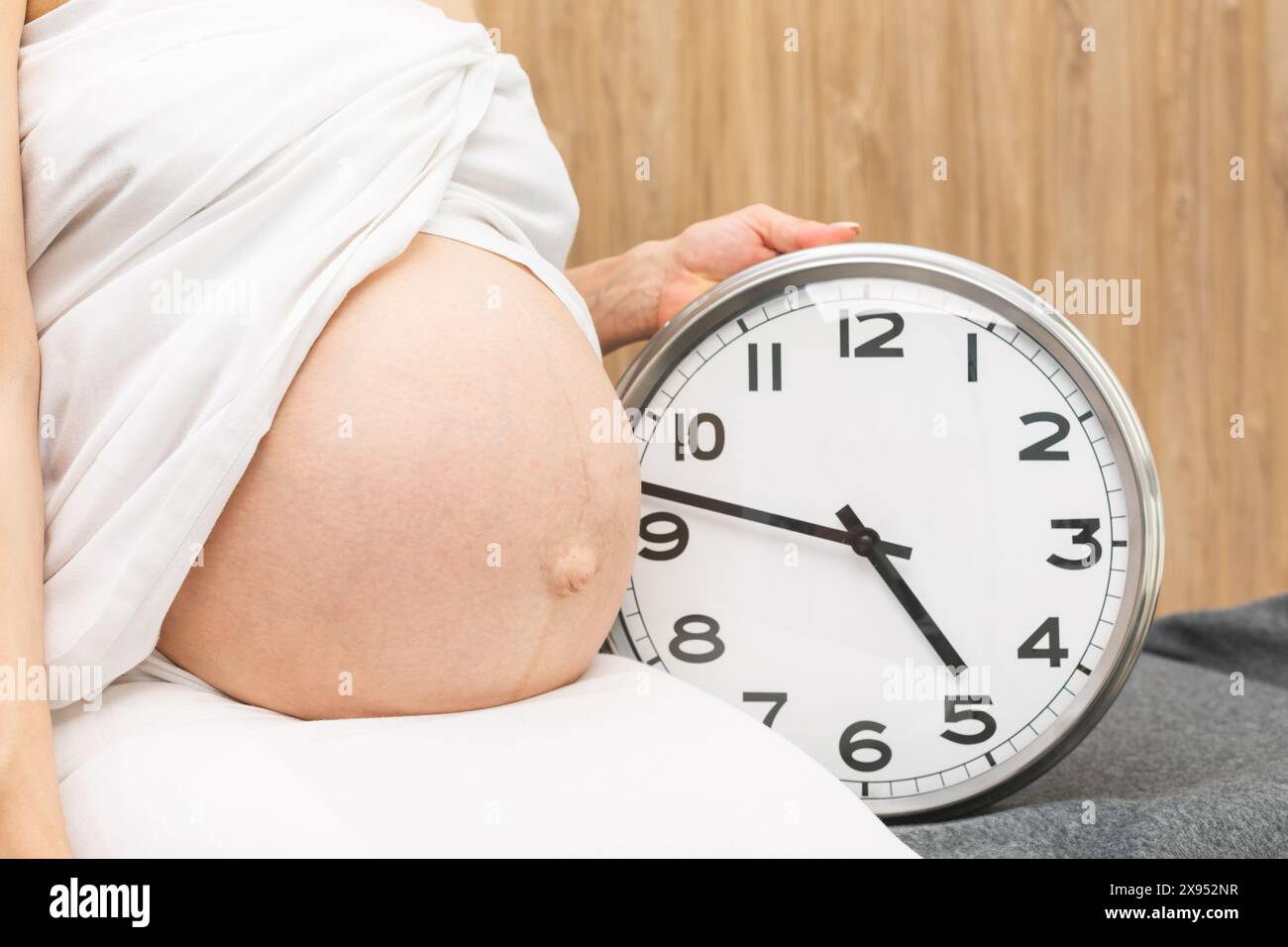 Femme enceinte assise avec horloge pendant les dernières semaines de grossesse Banque D'Images