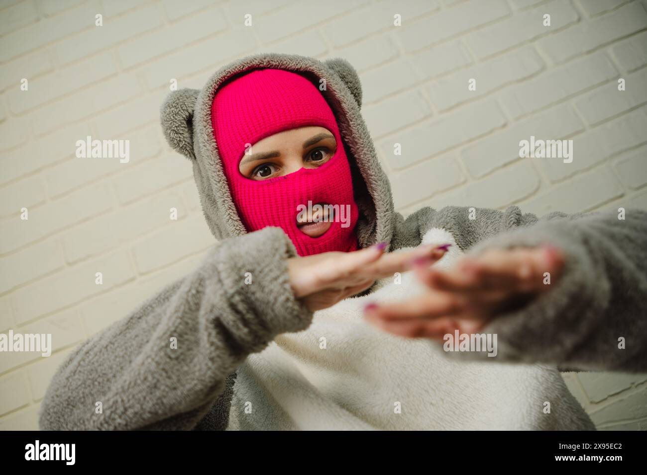 Femme en Balaclava rose dansant contre un mur de briques blanches Banque D'Images