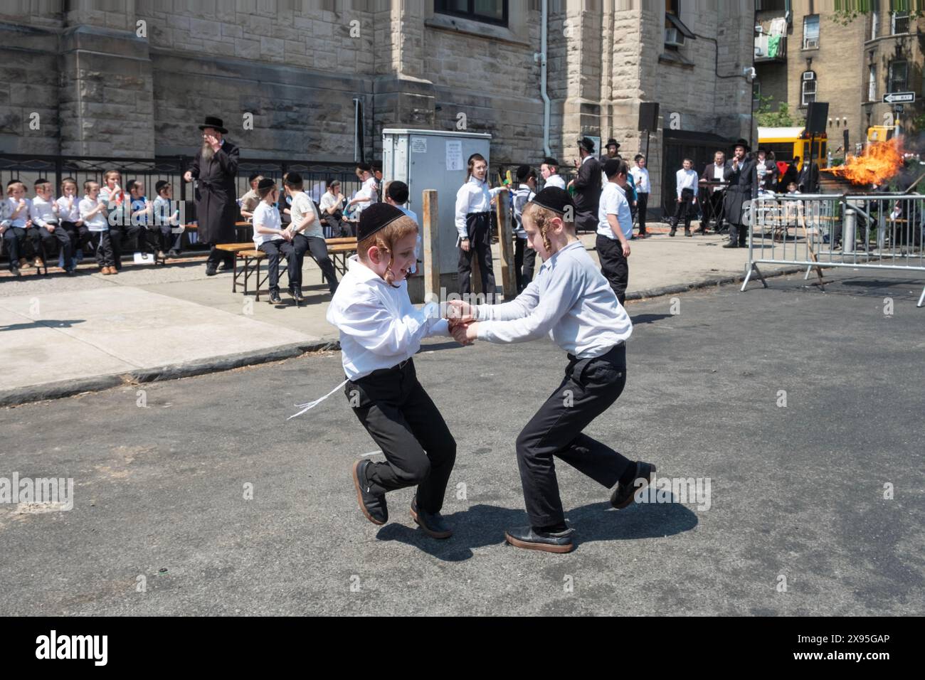 2 jeunes frères juifs hassidiques dansent ensemble lors d'une célébration du Lag B'Omer avec le feu traditionnel en arrière-plan. À Brooklyn, New York. Banque D'Images