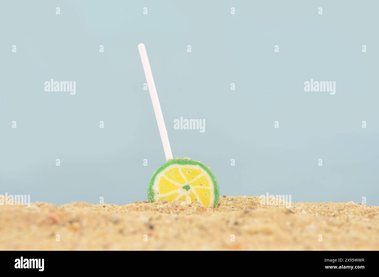 Sucette jaune et verte tombée sur une plage. Ciel bleu, sable jaune. Banque D'Images