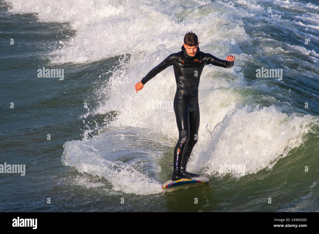 East Cliff Beach, Bournemouth - 14 mai 2024 : surfeur masculin debout sur une planche de surf sur une vague. Banque D'Images