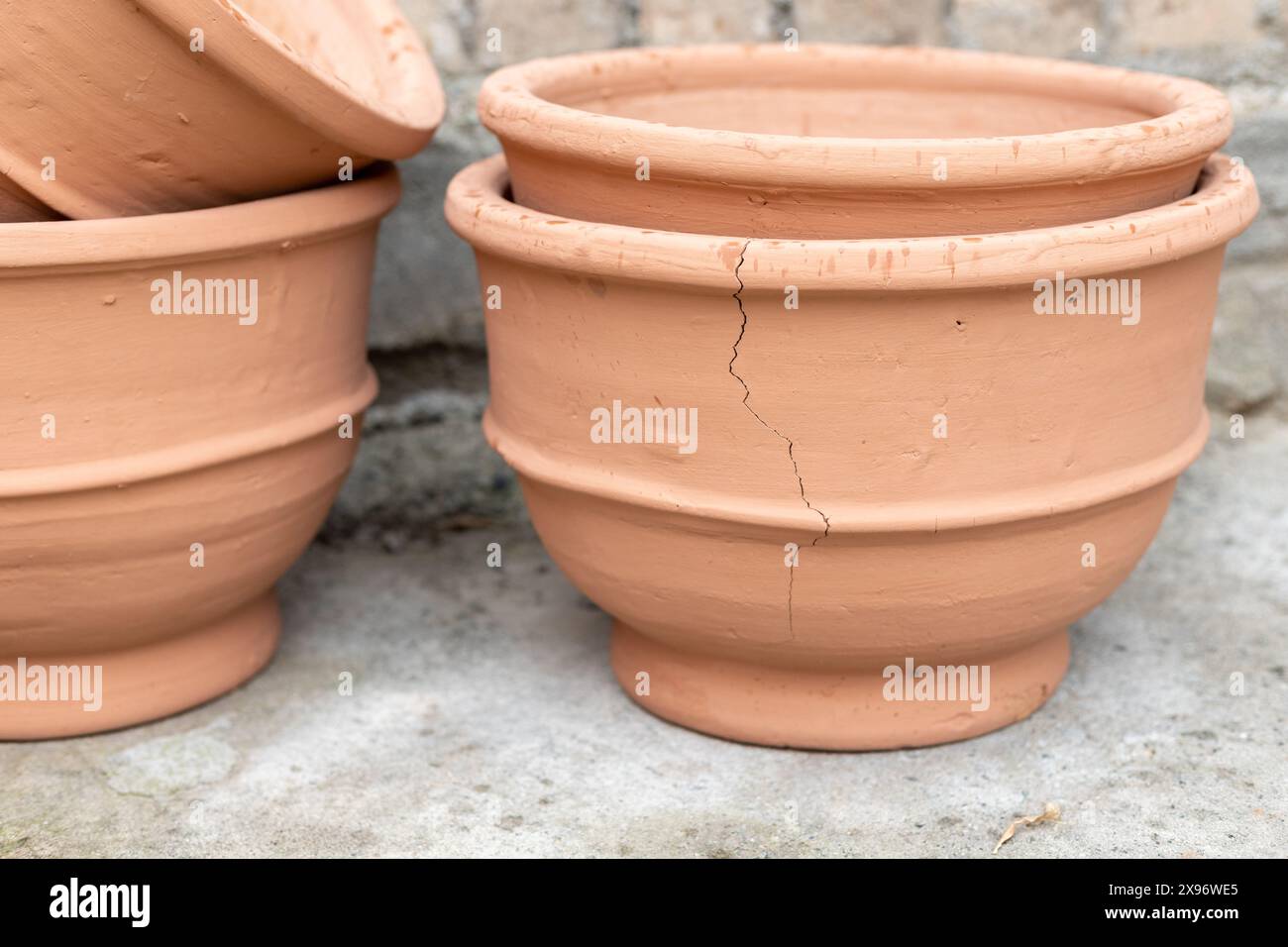 Pot de fleurs Crackederracotta. Une fissure visible coulant sur le côté. Les pots sont empilés sur une surface en béton avec un mur de briques en arrière-plan. Banque D'Images