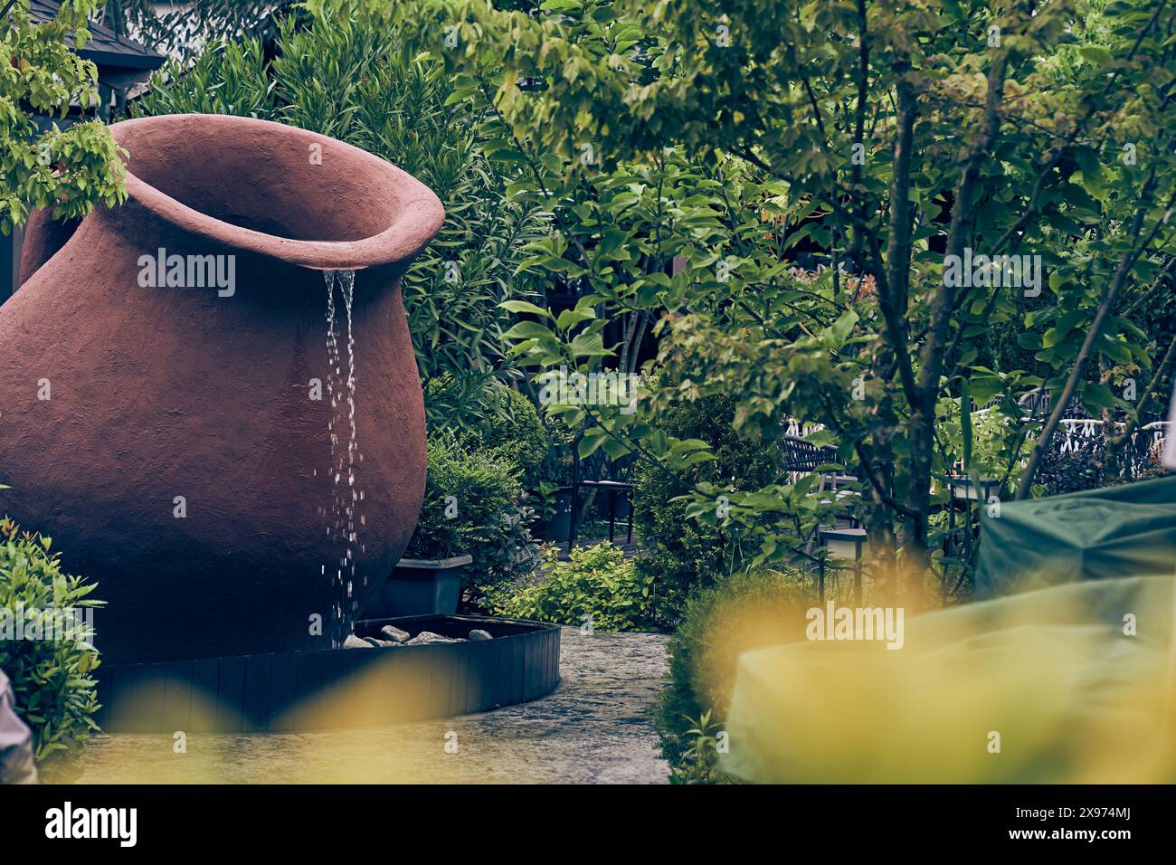 L'eau est versée d'une grande cruche décorative brune dans un récipient en dessous. une petite cascade près d'un café en plein air avec un espace copie. Photo de haute qualité Banque D'Images