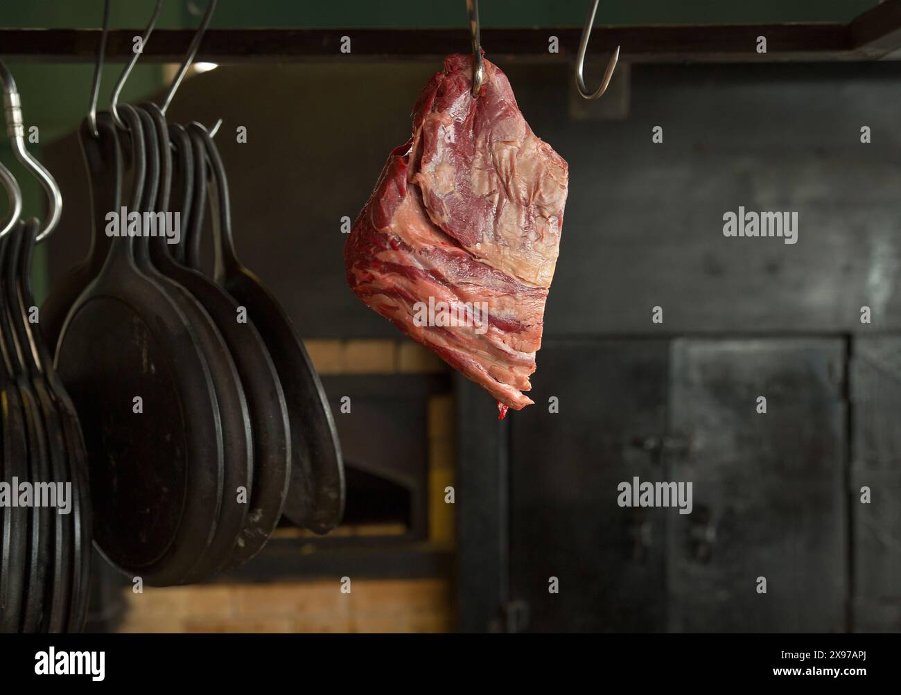 Morceau de viande sur un crochet avec des casseroles sur le fond d'un grand poêle noir Banque D'Images