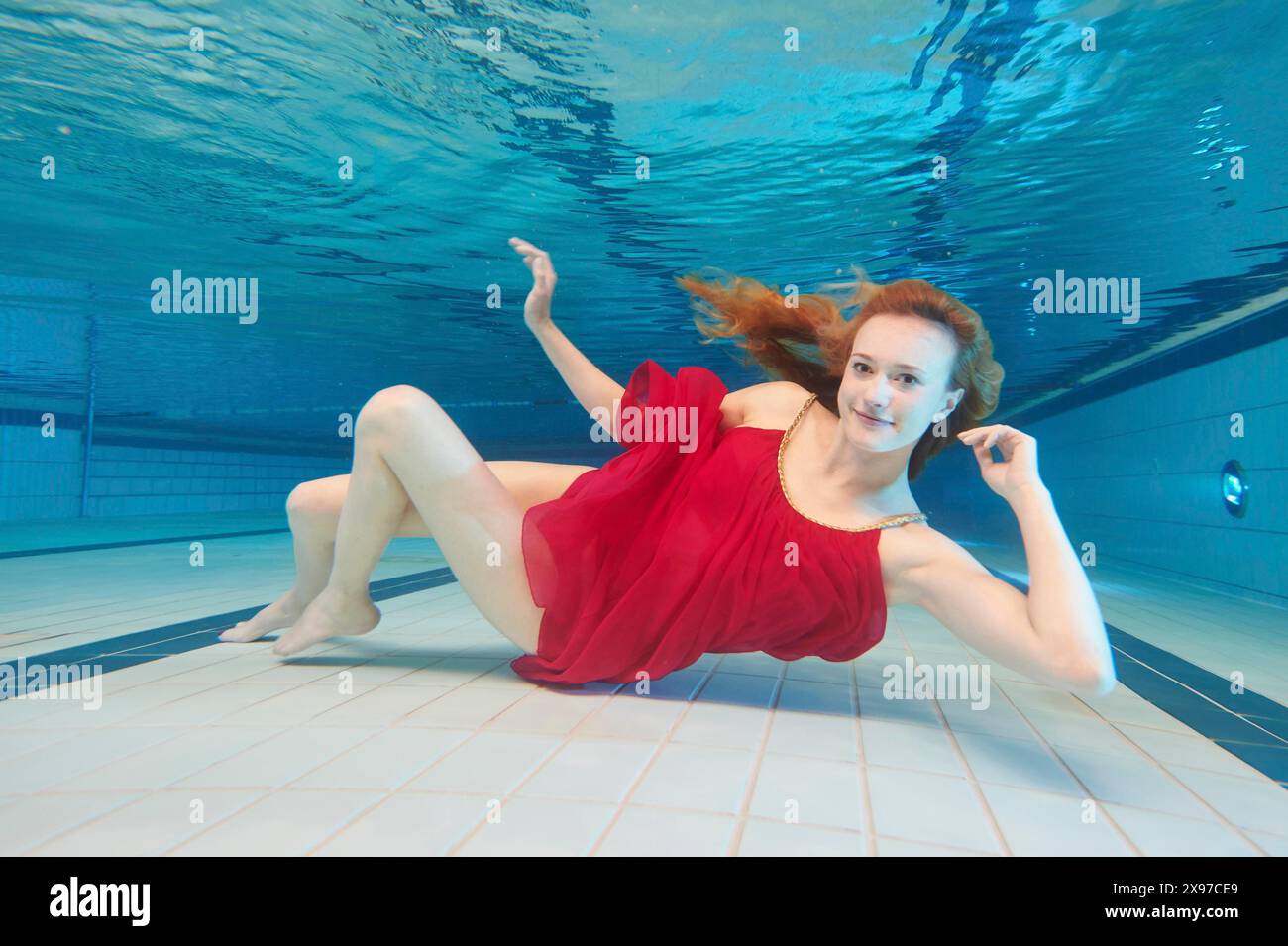 Une jeune femme avec une robe rouge plongeant sous l'eau dans un bain de natation Banque D'Images