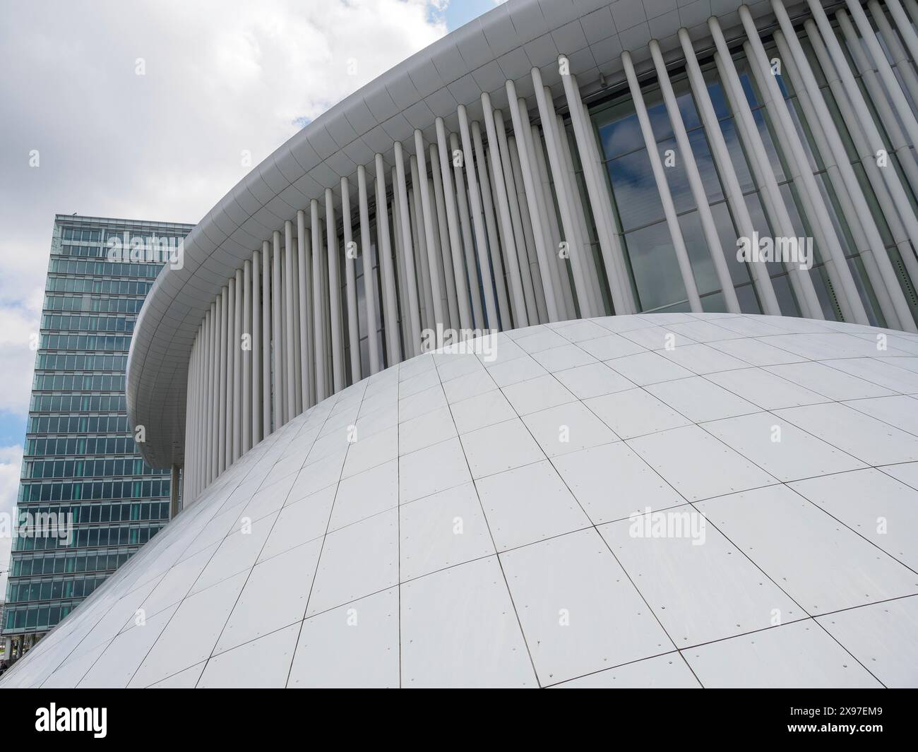 Structure blanche et incurvée devant une façade en verre moderne sous un ciel nuageux, bâtiments modernes avec arbres et façades en verre, luxembourg Banque D'Images