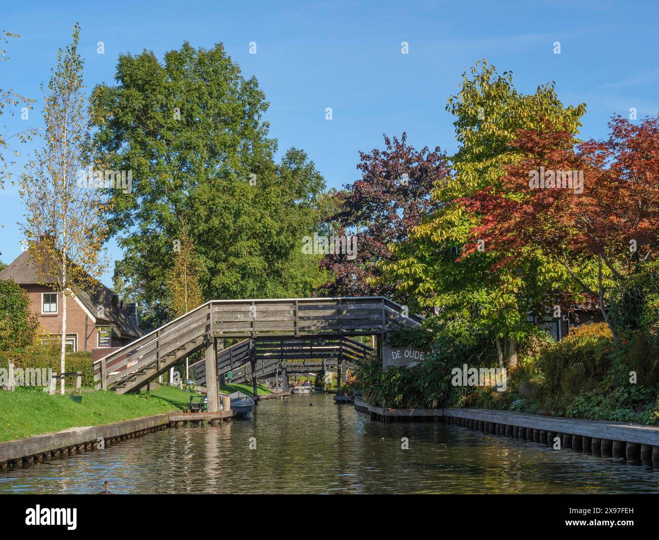 Une rivière tranquille avec un pont en bois voûté et un feuillage couleur automne, de petits ponts en bois sur les canaux aux pays-Bas, des maisons et des arbres sur Banque D'Images