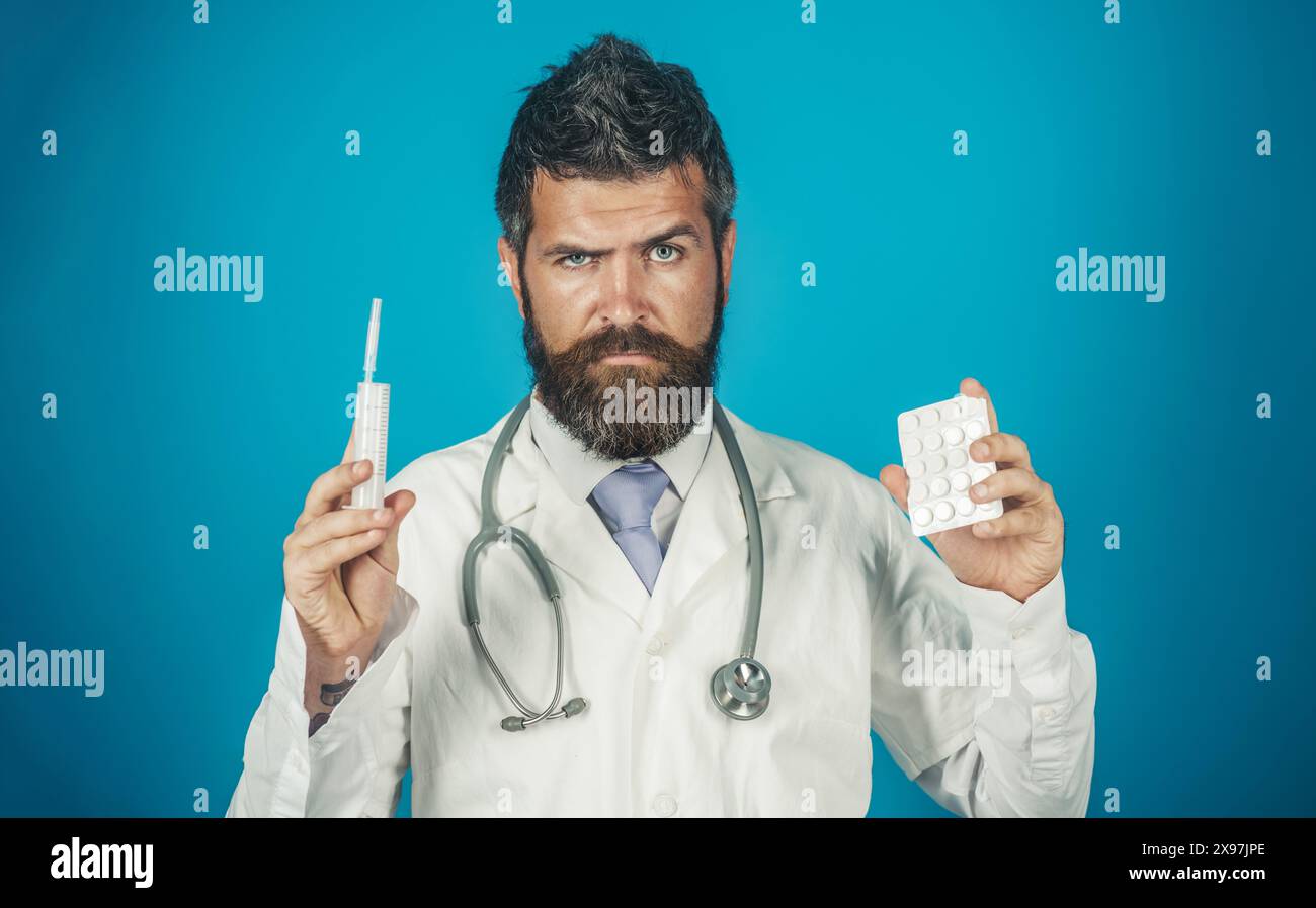 Médecin sérieux en manteau médical avec stéthoscope tient seringue et paquet de pilules. Infirmier masculin ou médecin avec injection médicale et blister avec Banque D'Images