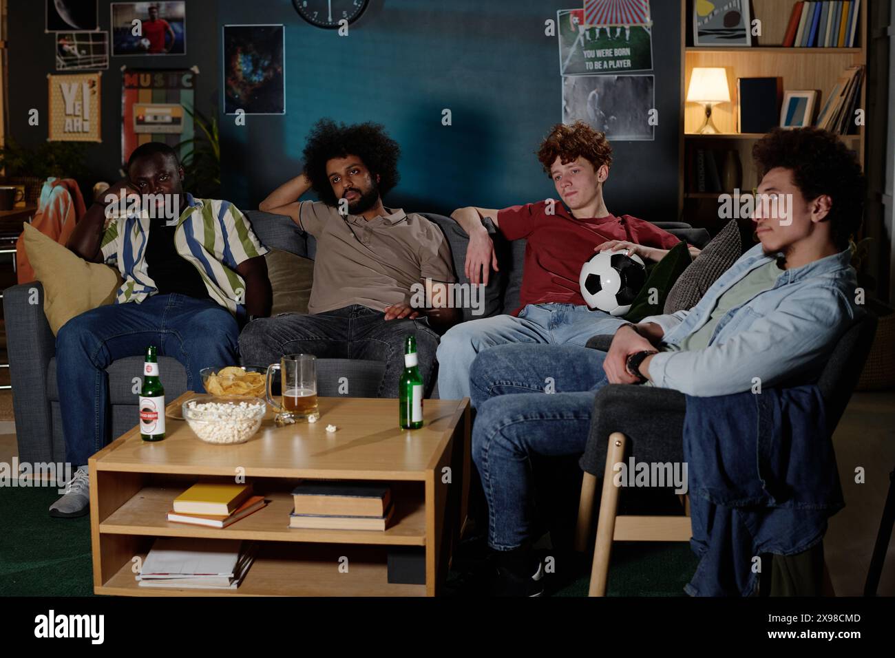 Groupe de jeunes hommes ethniquement diversifiés assis détendu sur le canapé dans le salon regardant la télévision tard dans la soirée, copie aspace Banque D'Images