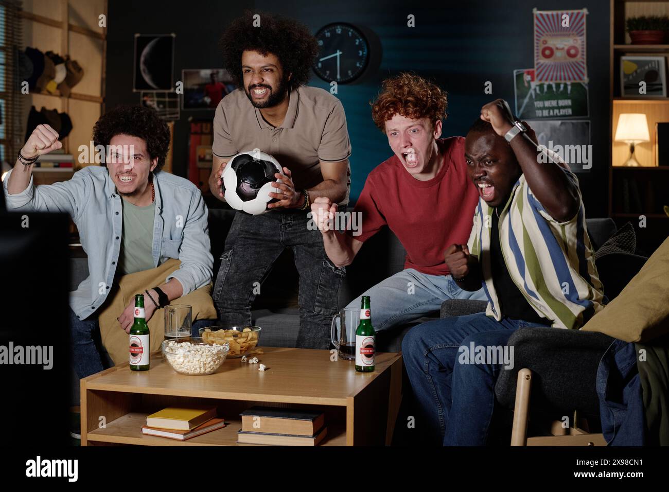 Groupe multi-ethnique de jeunes hommes excités passant la soirée ensemble dans le salon à regarder un match de football Banque D'Images