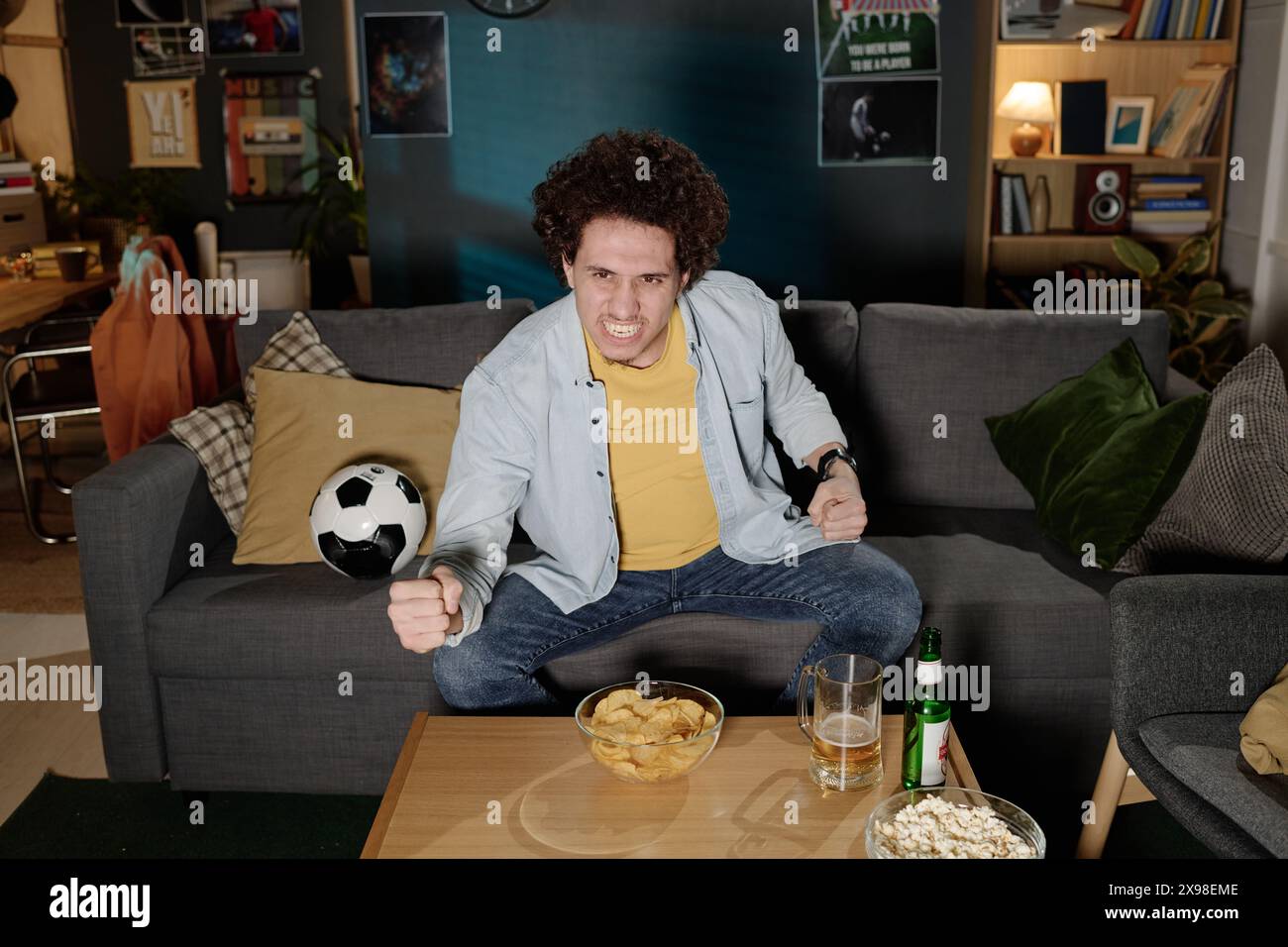 Vue en angle élevé d'un jeune fan de football biracial assis sur le canapé dans le salon regardant le match à la télévision tard dans la soirée Banque D'Images