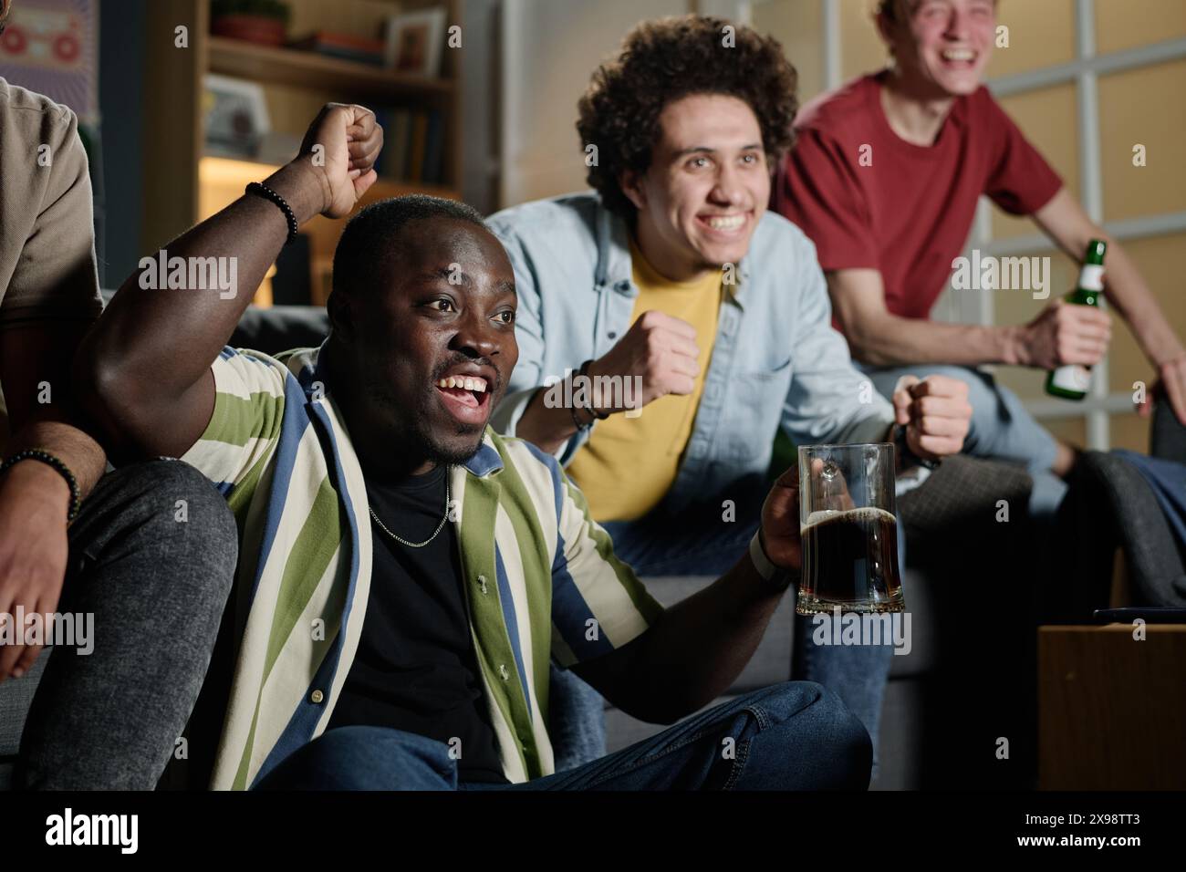 Jeune homme afro-américain et ses amis multi-ethniques s'amusant à regarder un match de football à la télévision dans la soirée Banque D'Images