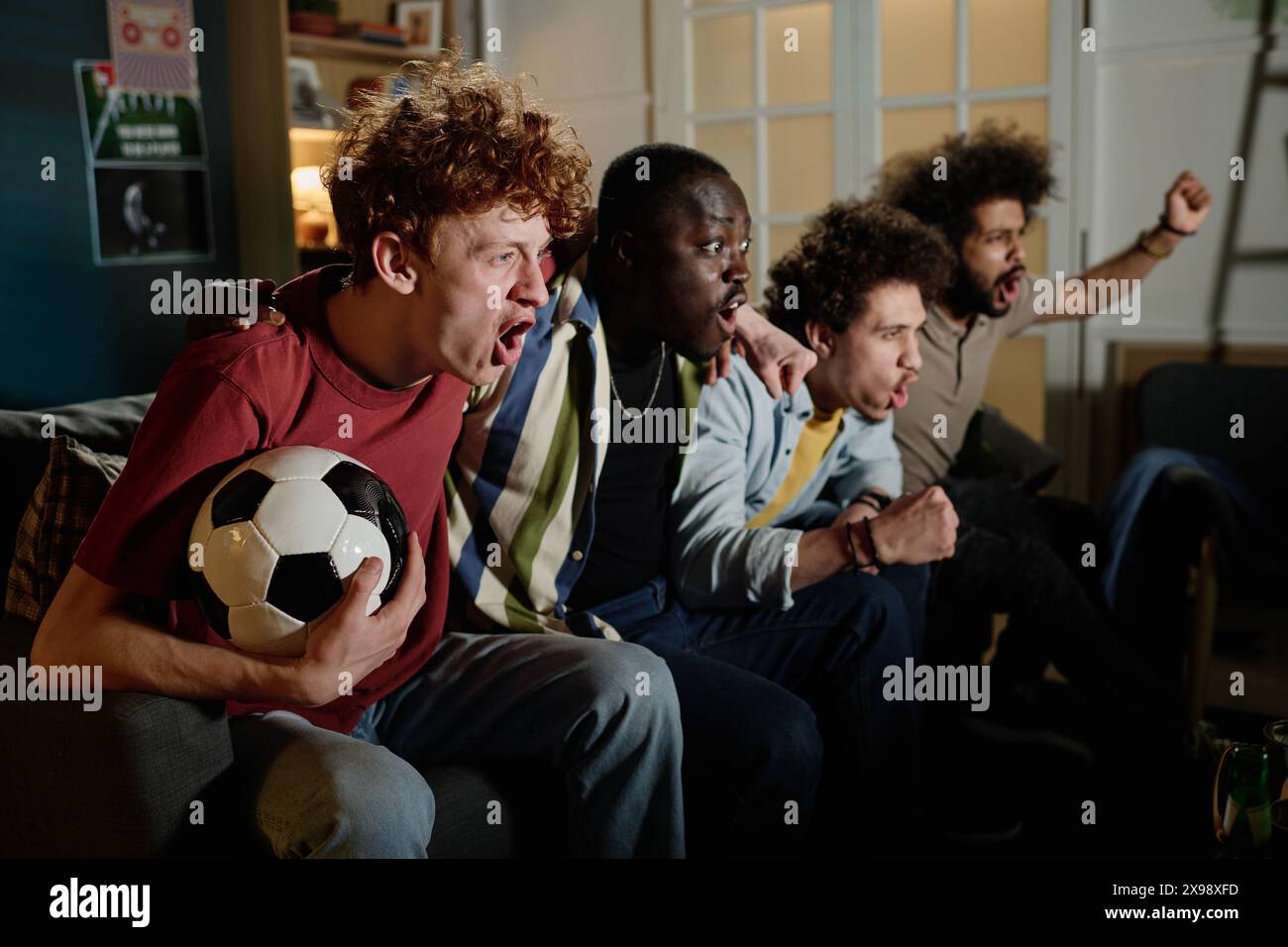 Groupe multi-ethnique de jeunes fans de football masculins assis sur le canapé dans le salon regardant le match à la télévision Banque D'Images