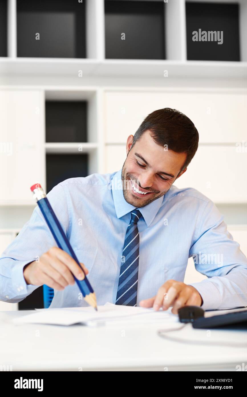 Bureau, sourire et homme d'affaires avec grand crayon par bureau pour la finance d'entreprise, la planification et les notes. Heureux, l'homme et l'écriture sur papier au lieu de travail pour Banque D'Images