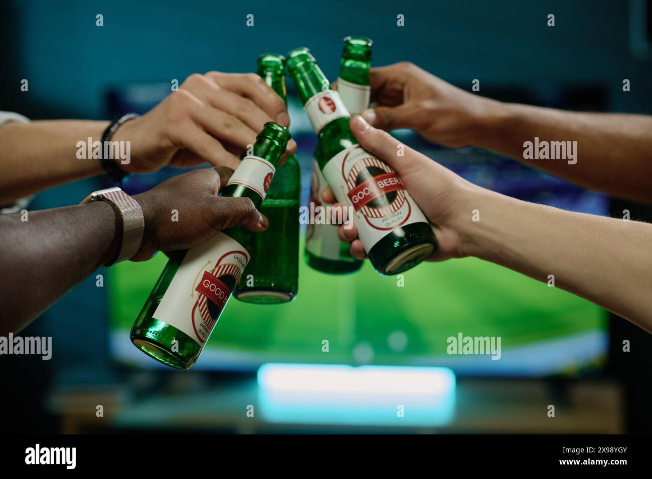 Gros plan des mains d'hommes méconnaissables serrant des bouteilles avec de la bière tout en regardant un match de football à la télévision Banque D'Images