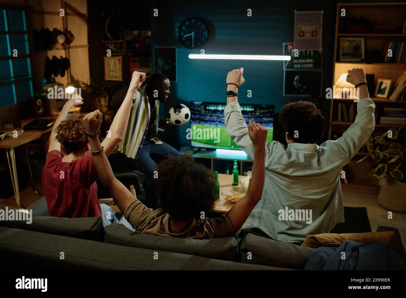 Vue arrière de quatre jeunes amis masculins appréciant de regarder un match de football à la télévision tard dans la soirée Banque D'Images
