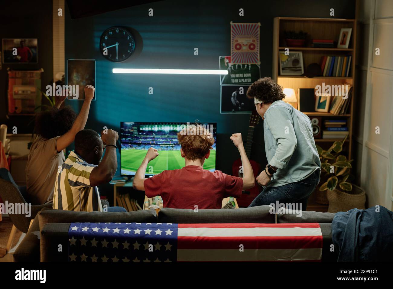 Vue arrière d'amis masculins ethniquement diversifiés passant la soirée dans le salon à regarder un match de football à la télévision, espace de copie Banque D'Images