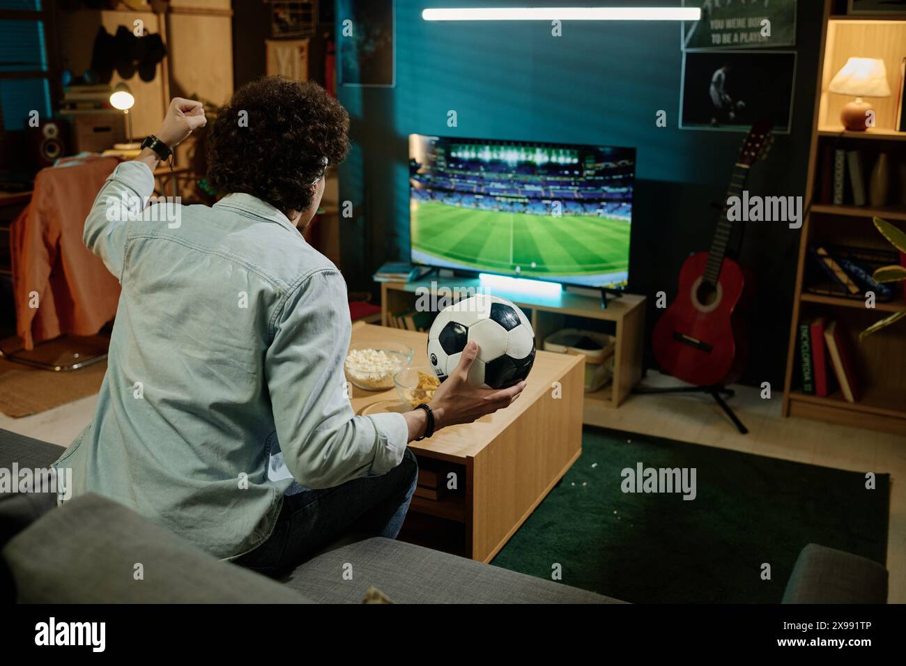Homme biracial méconnaissable tenant la balle assise sur le canapé dans le salon regardant le match de football à la télévision, espace de copie Banque D'Images