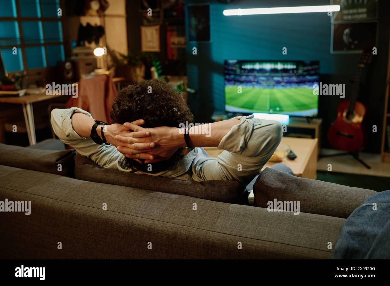 Vue arrière d'un homme méconnaissable assis détendu dans le salon regardant un événement sportif sur la chaîne de télévision, espace de copie Banque D'Images