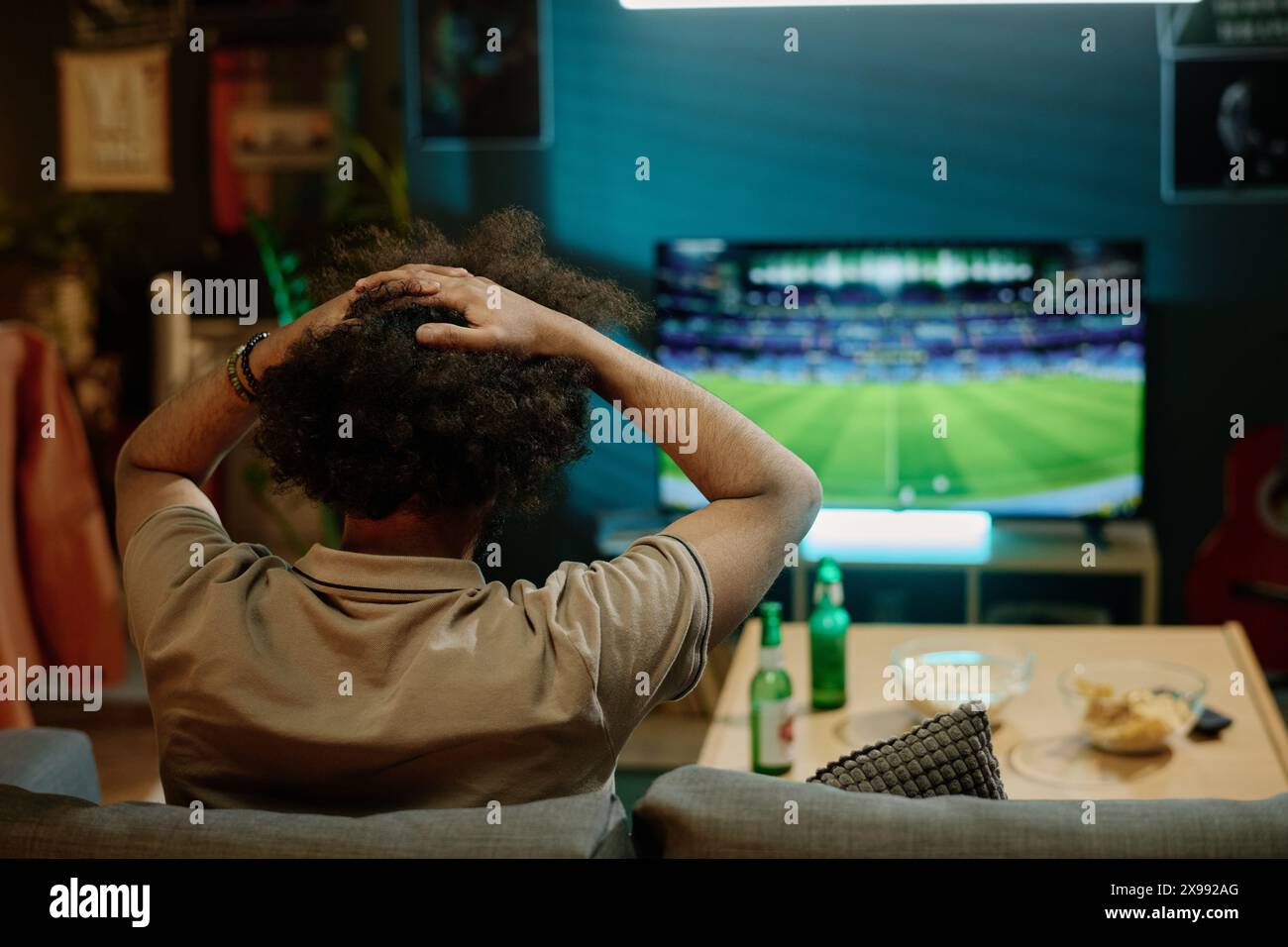 Vue arrière de l'homme méconnaissable déçu regardant un match de football à la télévision dans le salon à la maison, espace de copie Banque D'Images