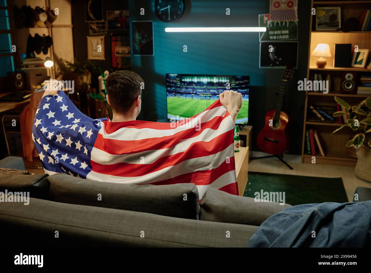 Vue arrière de l'homme méconnaissable avec drapeau assis sur le canapé regardant l'événement sportif à la télévision dans la soirée Banque D'Images