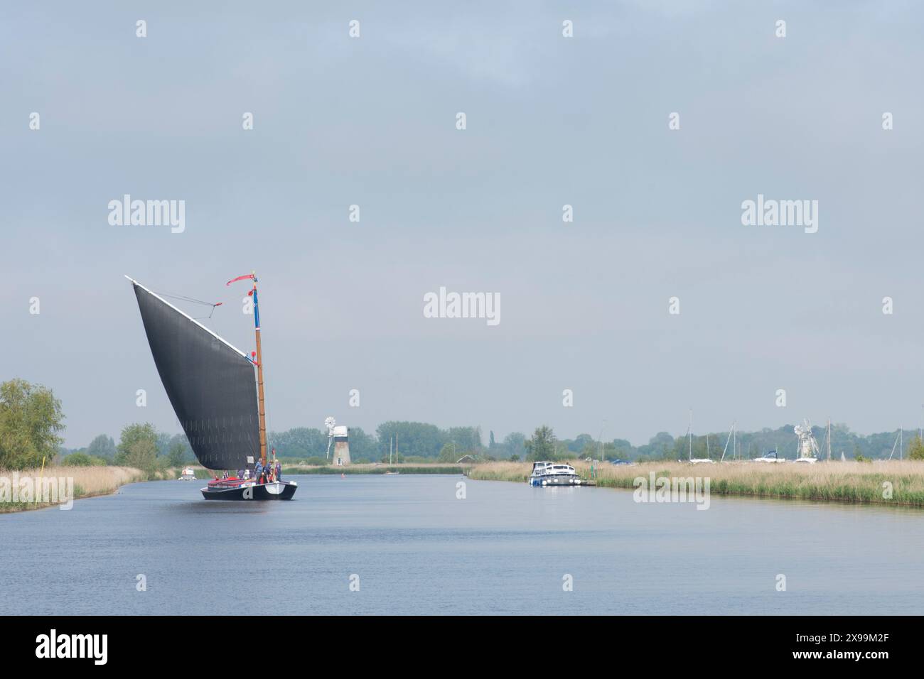 Les gens naviguent sur un bateau à voile traditionnel sur la rivière Bure, montrant St Benet's drainage Mill, et Thurne Dyke drainage Mill Banque D'Images