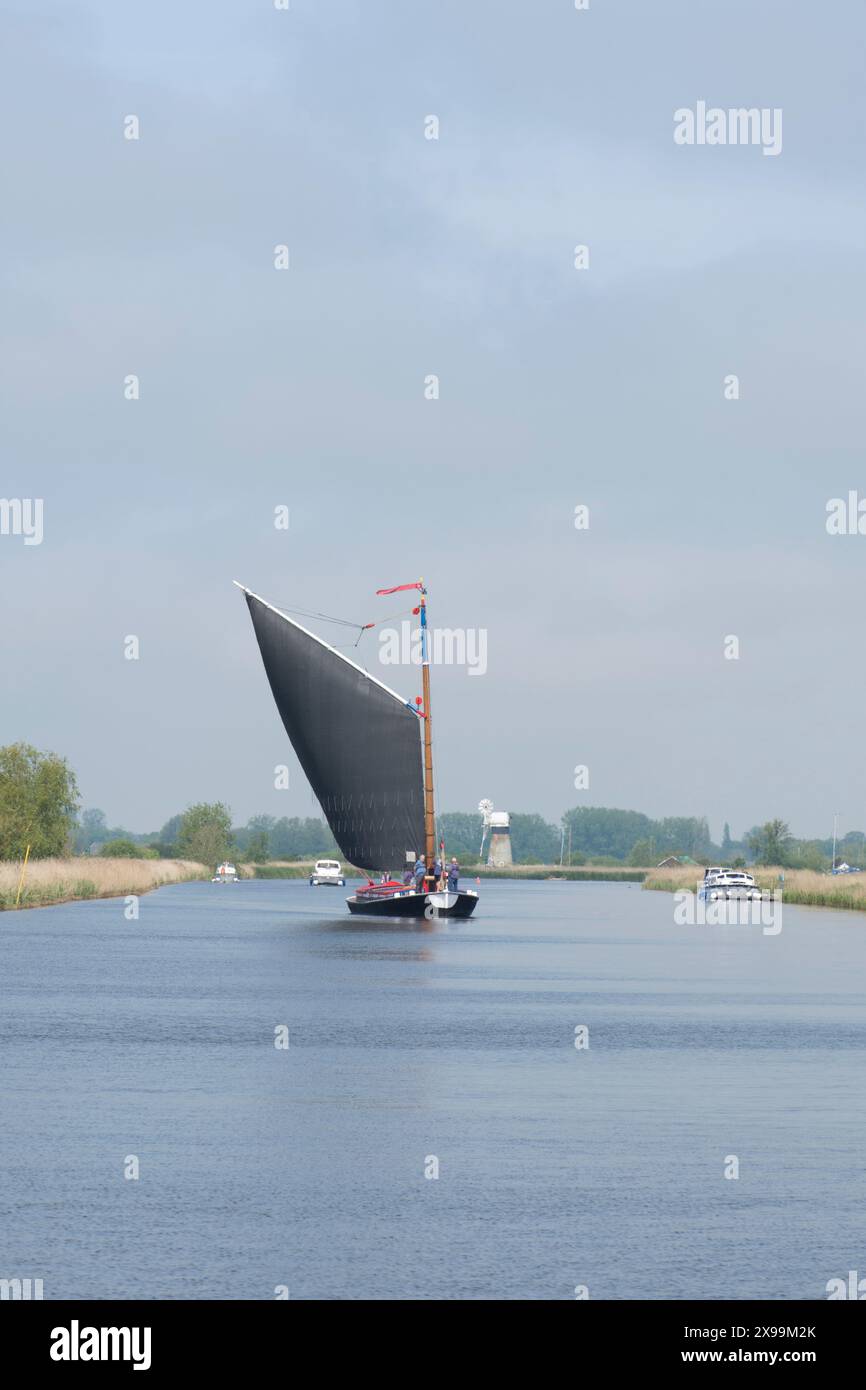 Les gens naviguent sur un bateau à voile traditionnel sur la rivière Bure, montrant St Benet's drainage Mill Banque D'Images