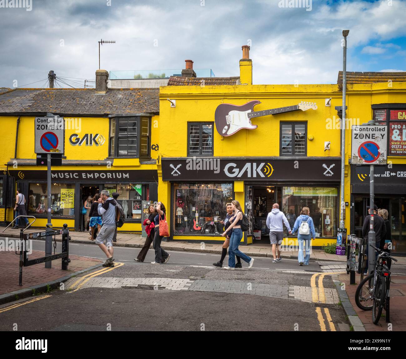 Les gens passent devant le Gak Music Emporium peint en jaune et le magasin de guitares dans la zone de conservation de Lanes à Brighton, East Sussex, Royaume-Uni. Banque D'Images