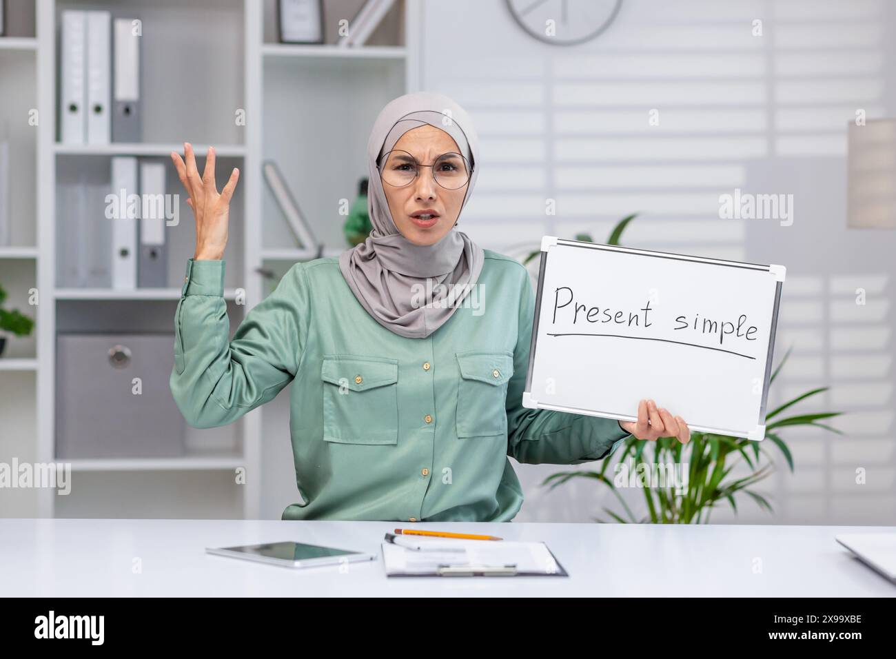 Enseignant expliquant le temps simple présent, tenant un tableau blanc en classe, exprimant la frustration ou la confusion, dans un environnement éducatif moderne. Banque D'Images