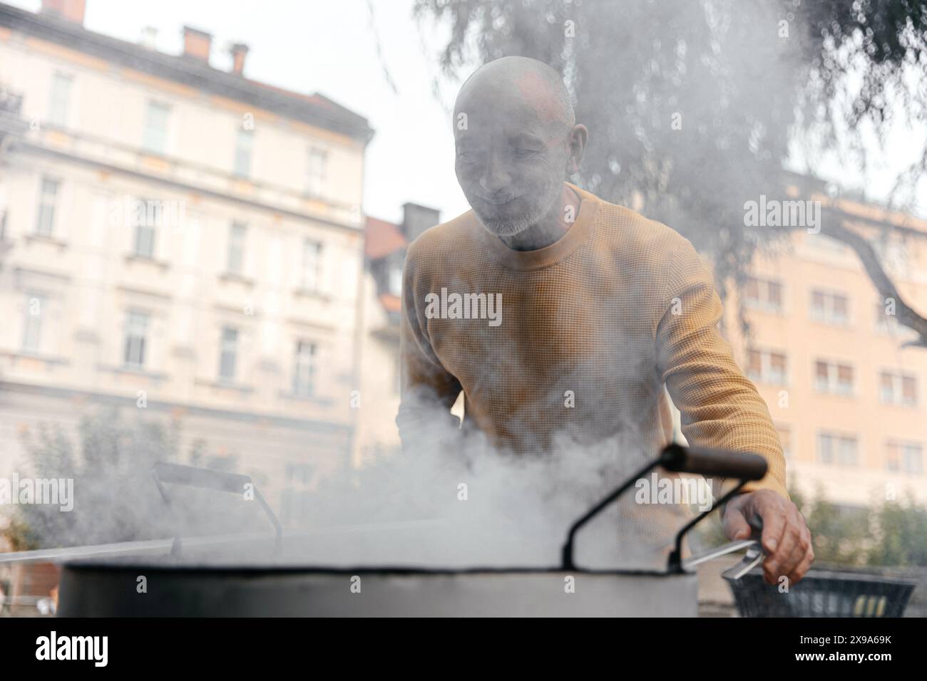 Homme senior en pull jaune souriant près de Cooking pot sur Urban Street Banque D'Images