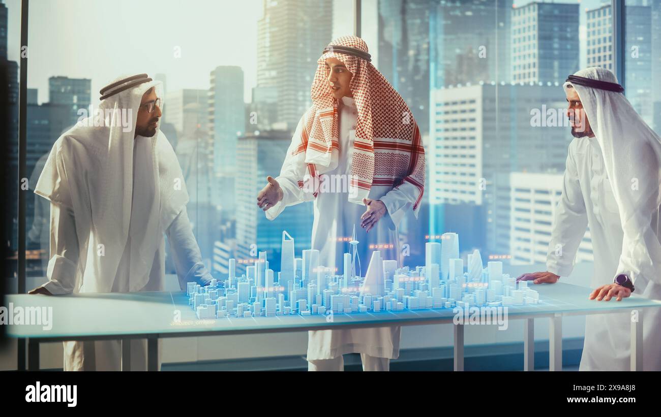 Groupe de développeurs d'affaires immobilières arabes dans les vêtements traditionnels discutent des opportunités d'investissement basées sur le modèle de ville 3D de réalité augmentée holographique dans leur bureau moderne dans un gratte-ciel. Banque D'Images