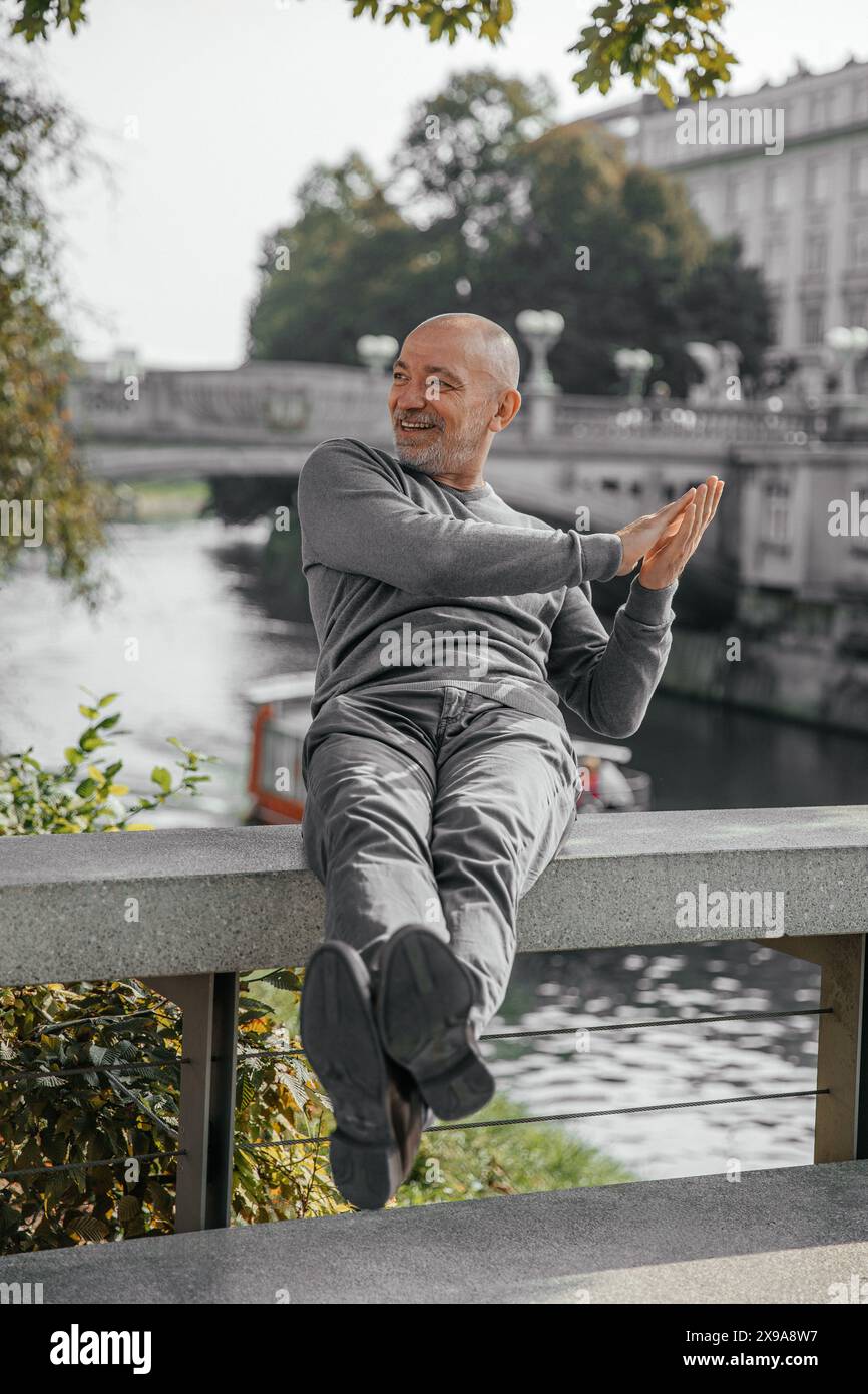 Heureux homme senior en pull gris assis sur un banc, souriant et applaudissant les mains Banque D'Images