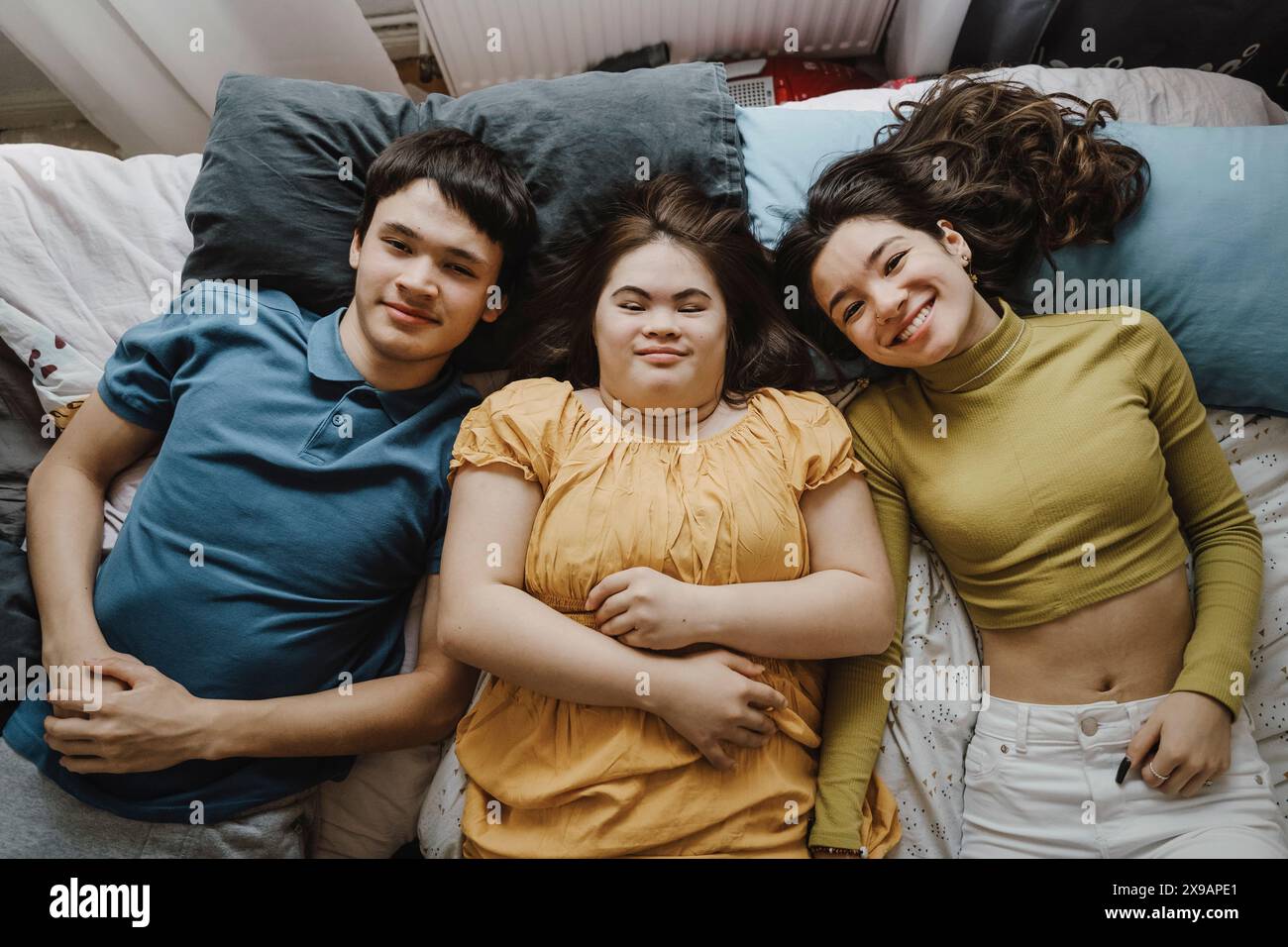 Portrait d'heureux frères et sœurs masculins et féminins couchés à côté de la sœur avec le syndrome de Down sur le lit à la maison Banque D'Images
