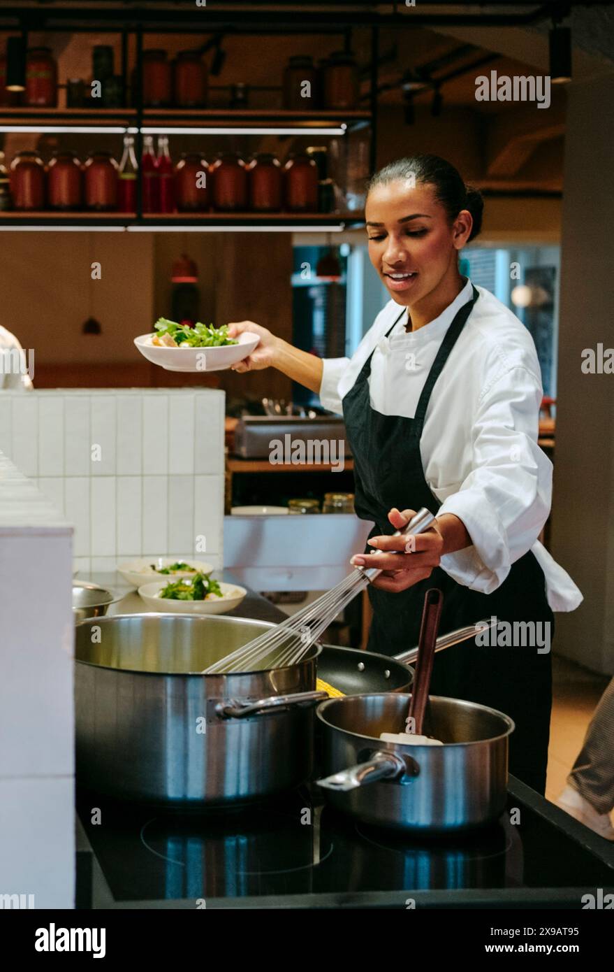 Femme chef remuant avec un fouet métallique tout en tenant un saladier dans la cuisine commerciale Banque D'Images