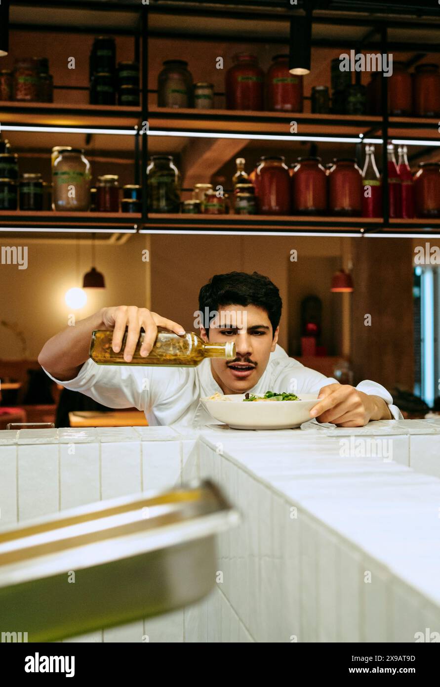 Chef masculin concentré versant de l'huile de vinaigrette dans un saladier à la cuisine commerciale Banque D'Images