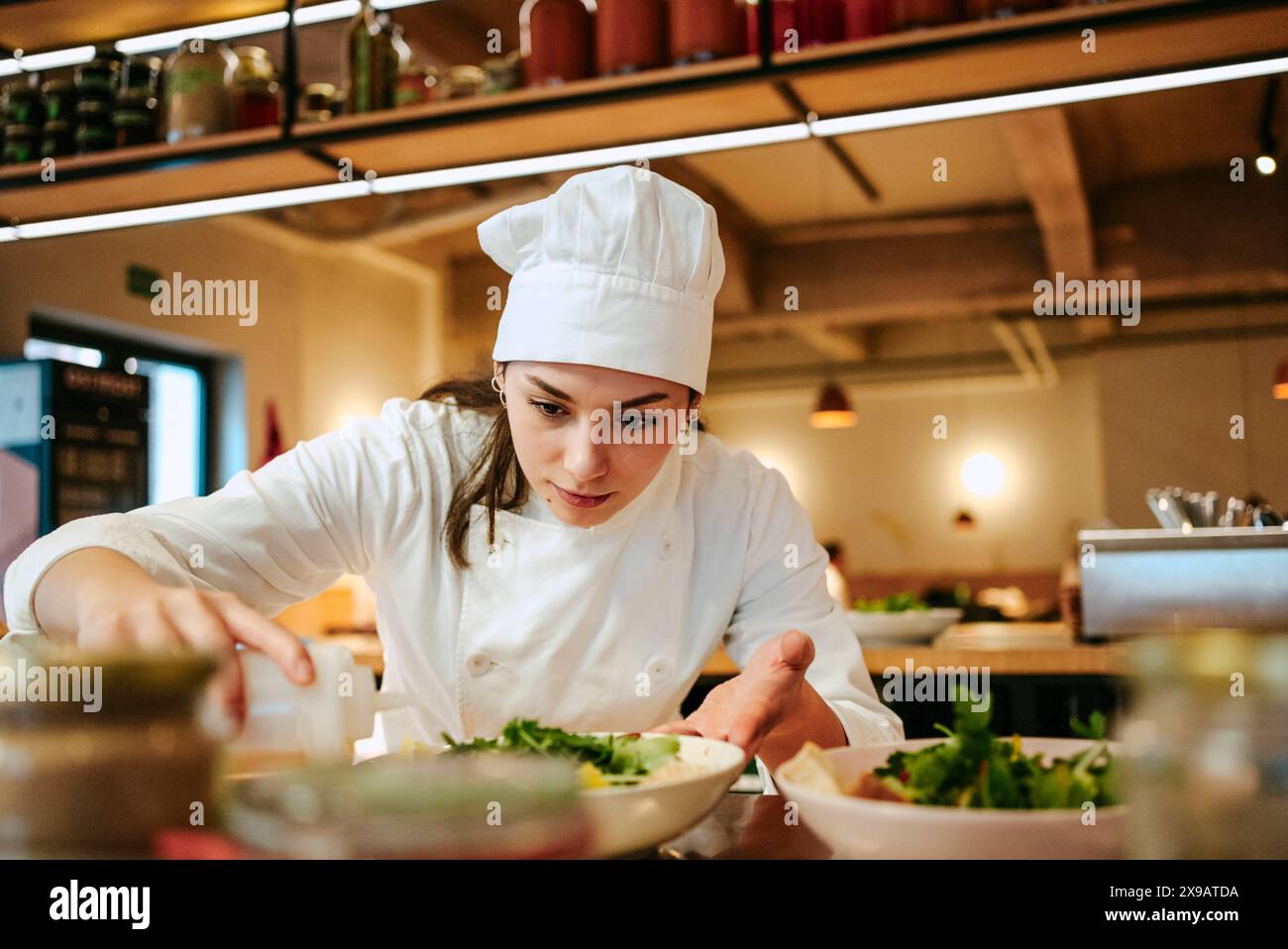 Gros plan d'une femme chef versant de l'huile de vinaigrette sur une salade à la cuisine commerciale Banque D'Images