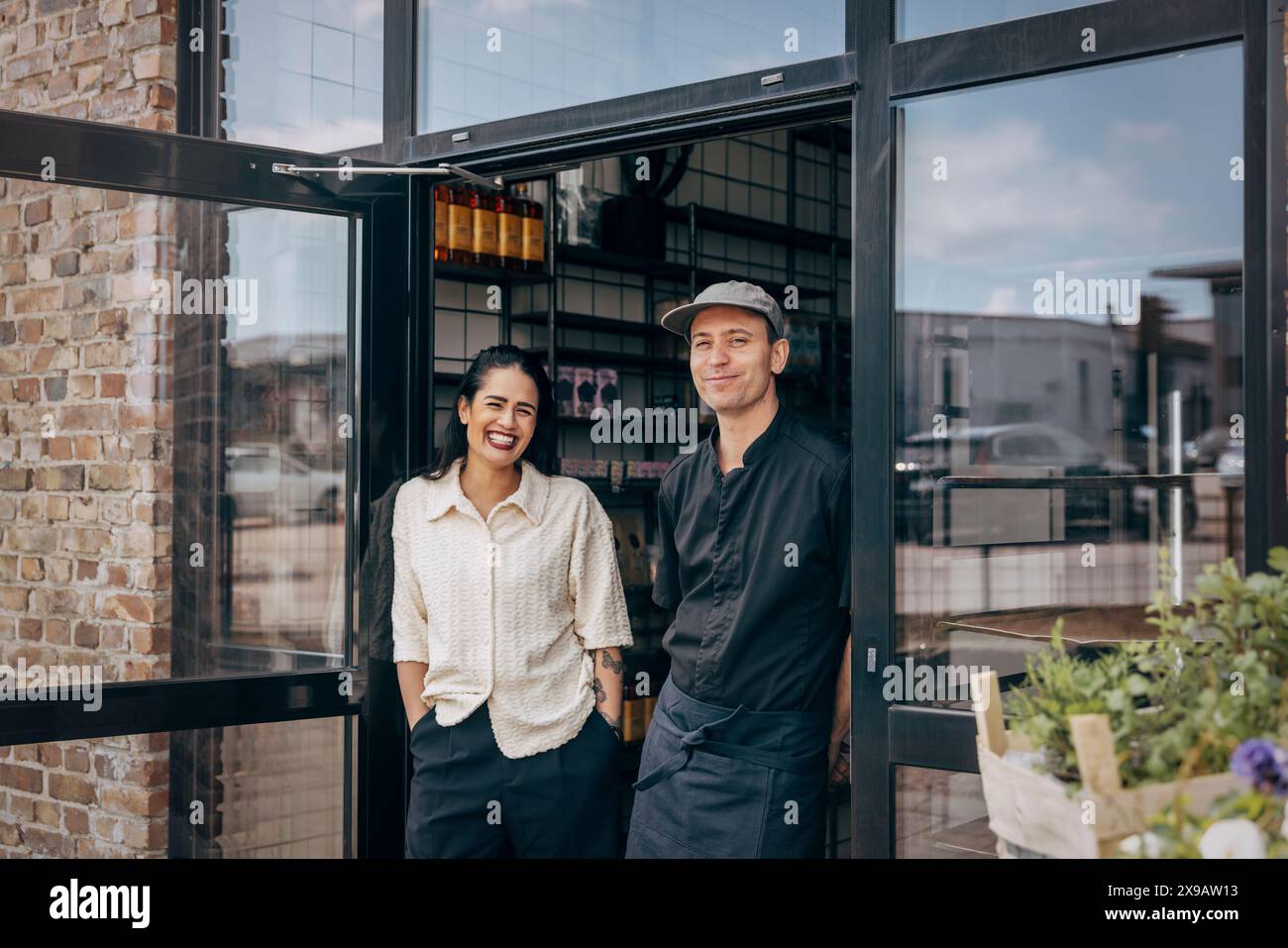 Propriétaire féminin heureux debout avec un collègue masculin à la porte du café Banque D'Images
