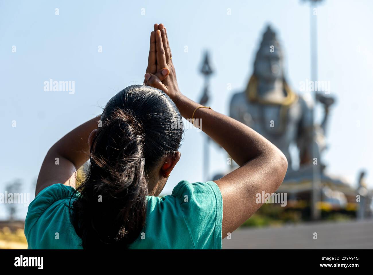 Une personne dans le traditionnel Anjali Mudra prie devant une majestueuse statue de divinité hindoue dans un temple serein. L'échafaudage de construction fait allusion à la rénovation en cours Banque D'Images